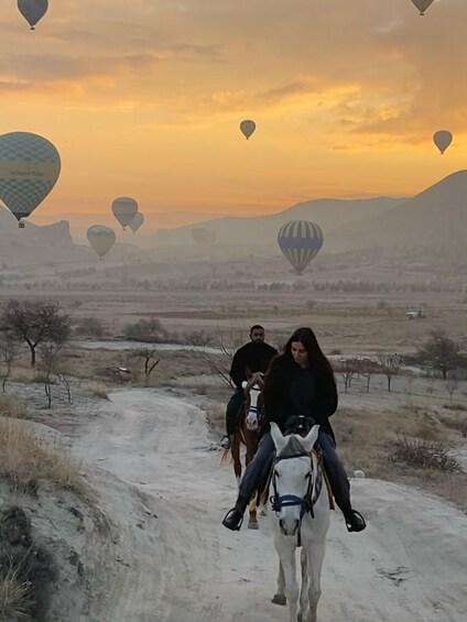 A person riding a horse on a dirt path with hot air balloons in the background. 4
