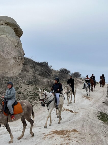 A group of people riding horses on a dirt path surrounded by rocky terrain and sparse vegetation. 1
