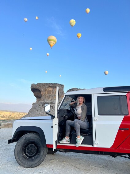 A vehicle with a person sitting in the driver's seat, a rocky outcrop in the background, and several hot air balloons in the sky. 5