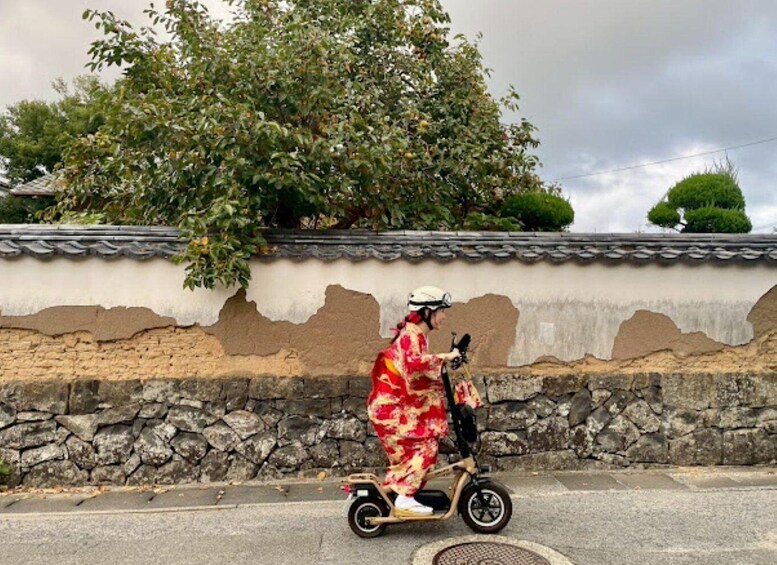 A person riding a scooter on a street with a traditional building and trees in the background. 5