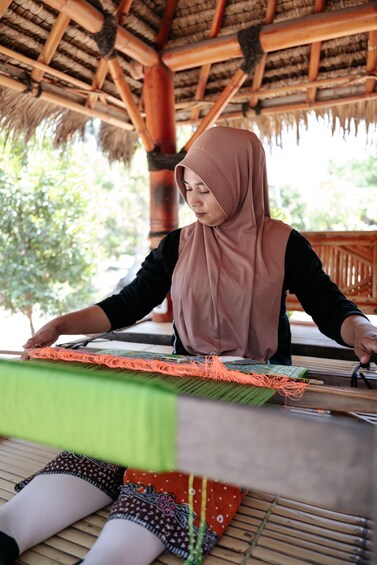 A person weaving on a loom under a thatched roof. 3