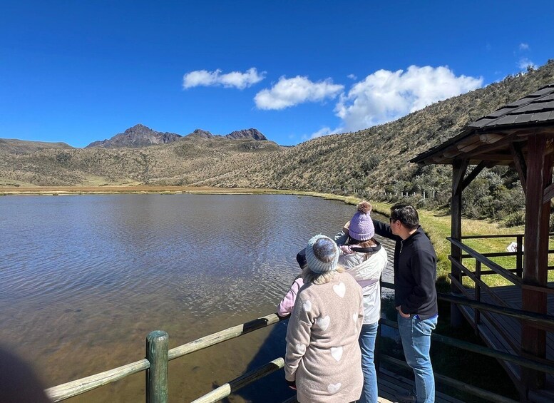 A group of people standing by a wooden dock overlooking a calm lake with mountains in the background. 5