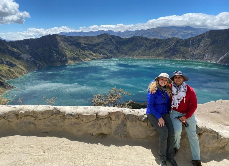 A couple sitting on a stone wall overlooking a turquoise lake surrounded by mountains. 1