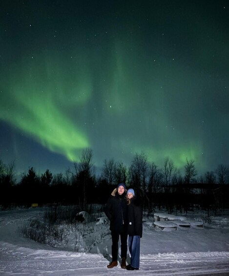 Two people standing in a snowy landscape under a night sky with the aurora borealis. 2