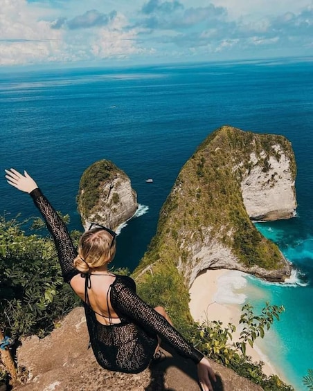 A person sitting on a cliff overlooking a coastal landscape with distinctive rock formations and a clear view of the ocean. 1