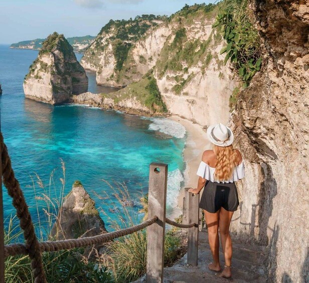 A person standing on a cliff overlooking turquoise waters and rocky cliffs. 5