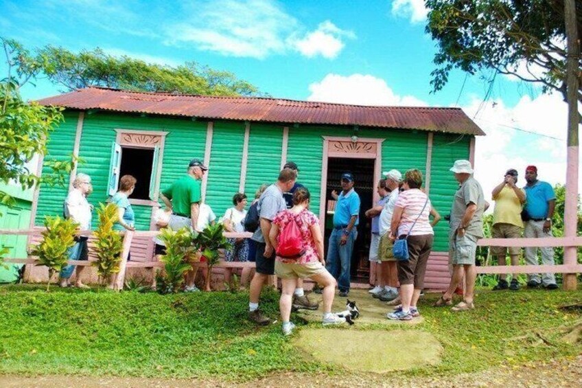 A group of people standing in front of a green wooden building with a red roof. 2