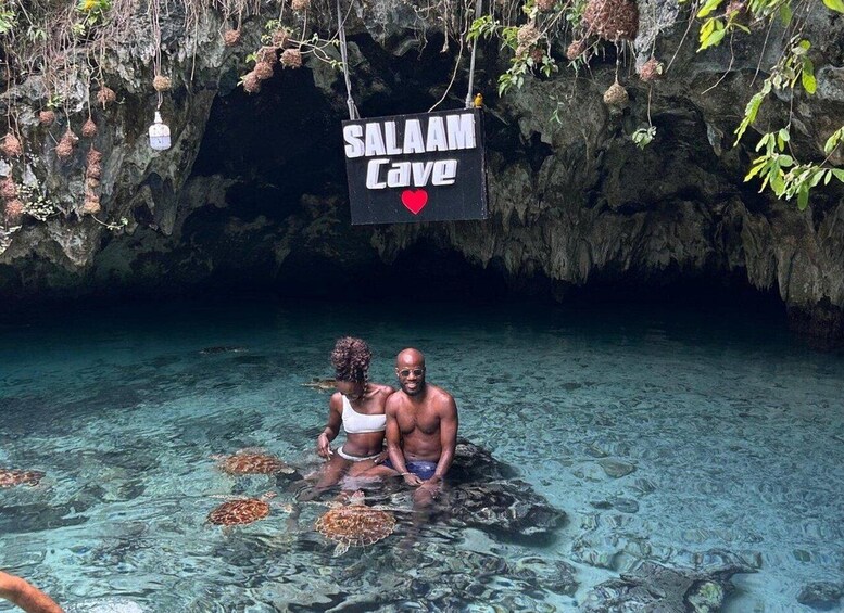 A couple in clear water with sea turtles, a cave entrance, and a sign reading 'SALAM Cave'. 1