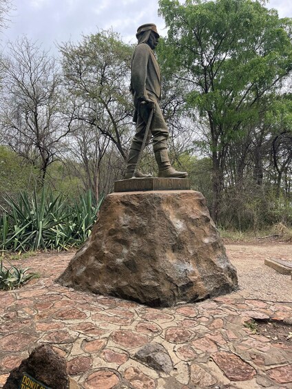 A statue of a man in military attire on a stone pedestal, surrounded by trees and greenery. 5