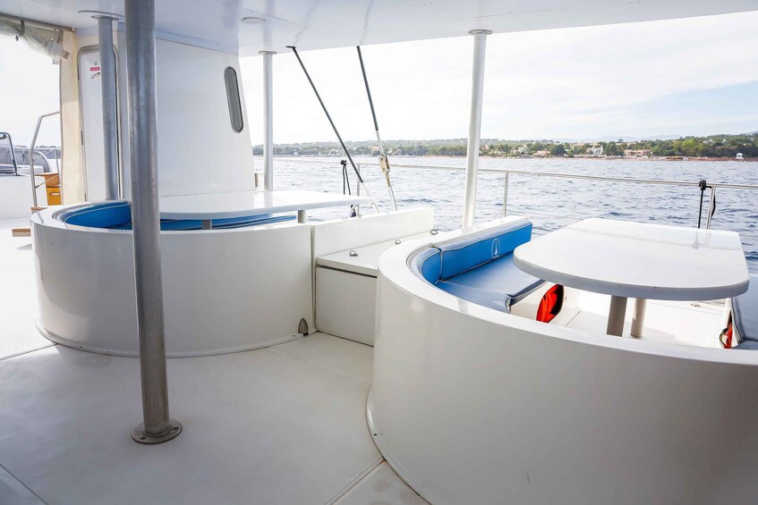 A boat deck with a white table, a blue cushioned seat, and a metal pole. 2