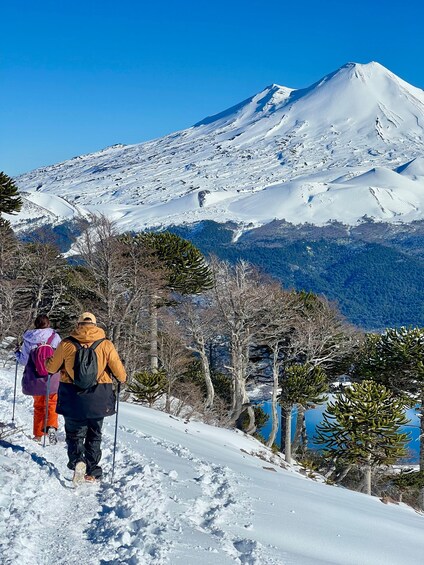 Two hikers on a snowy trail with a snow-covered mountain in the background. 1