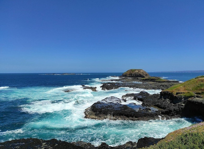 A rocky coastline with waves crashing against the rocks under a clear blue sky. 3