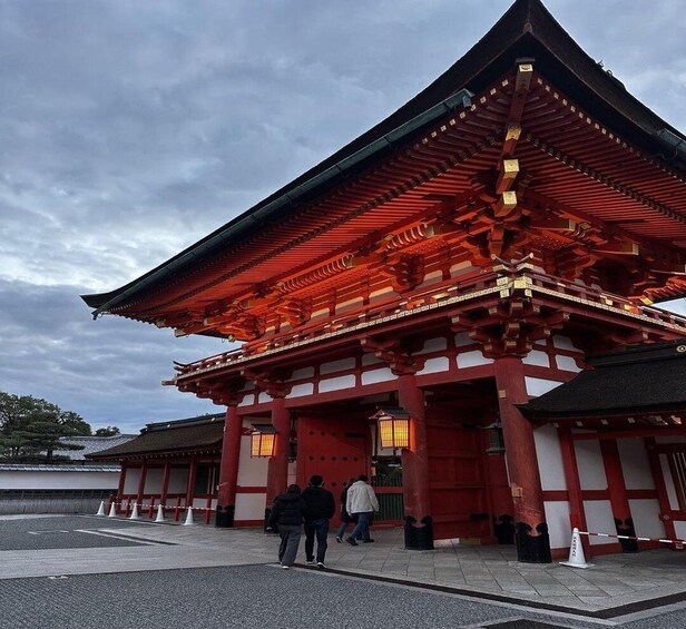 Perinteinen japanilainen temppeli, jossa on punaisia ja valkoisia rakennuksia, suuri portti ja ihmisiä kävelemässä sen edessä. 2