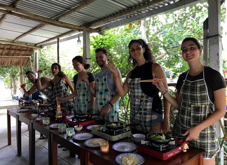A group of people cooking outdoors under a metal roof, with various cooking utensils and ingredients on the table. 1