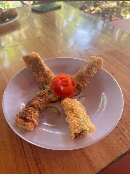 A plate with four breaded items and a cherry tomato on a wooden table. 2