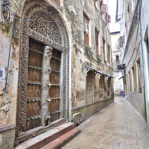 An ornate arched doorway with intricate carvings, a narrow alleyway, and a distant view of a building. 5