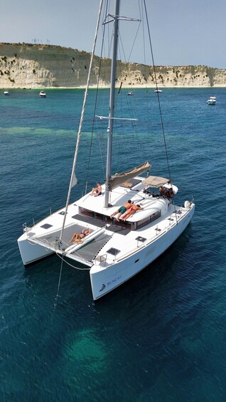 A white sailboat named SUNCAT anchored in clear blue waters with a rocky coastline in the background. 1