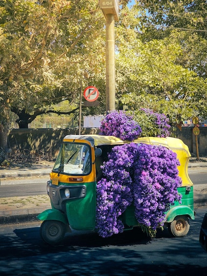 A green and yellow auto-rickshaw parked on the side of a road, covered with purple flowers. 3
