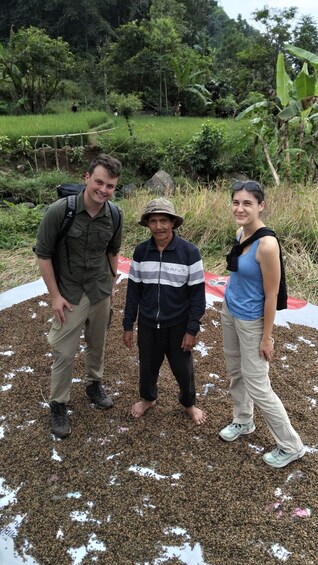 Three people standing on a field with scattered seeds and a red banner in the background. 1