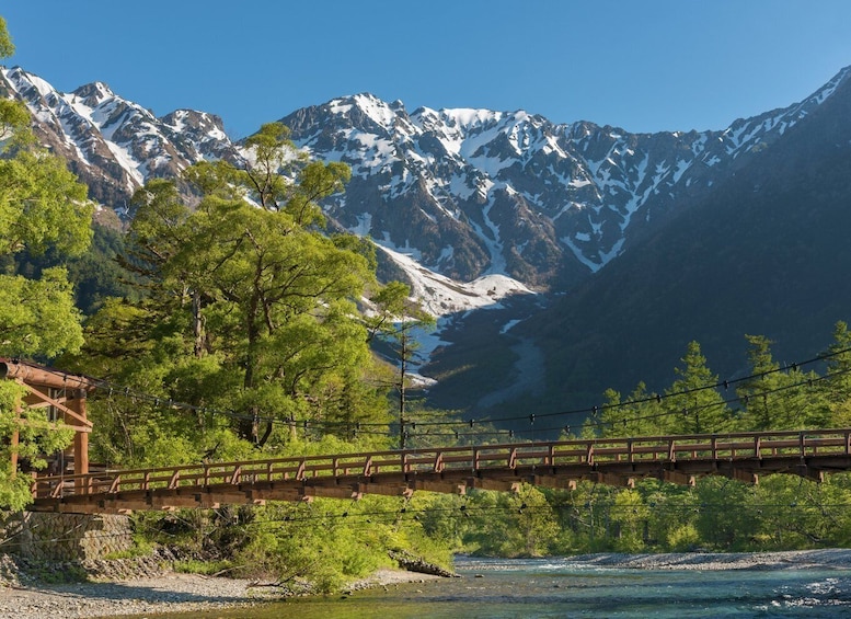 A wooden bridge over a river with snow-capped mountains in the background. 1