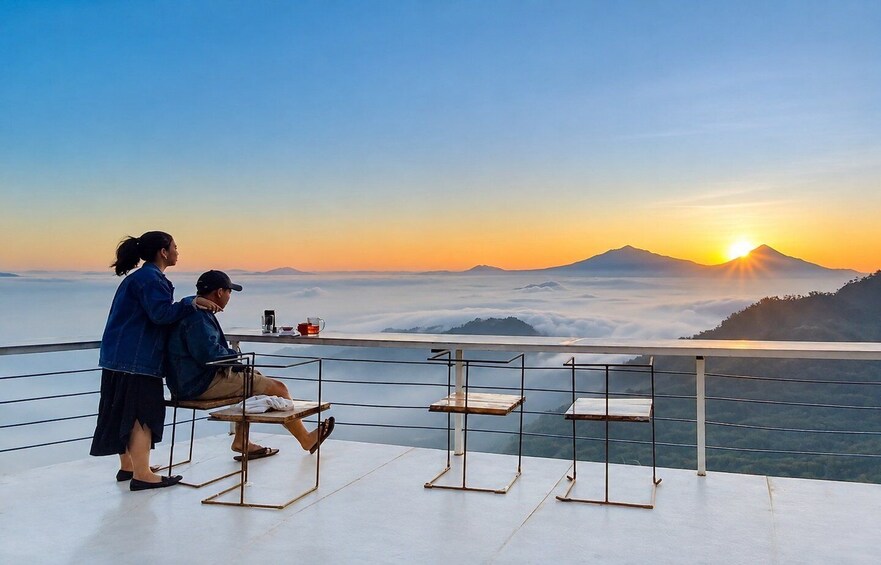 A couple sitting on a balcony overlooking a mountainous landscape at sunset. 1
