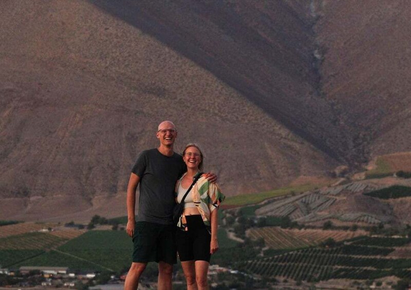 A man and a woman standing in a rural landscape with terraced fields and a mountain in the background. 2