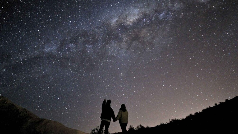 Two people holding hands under a starry night sky. 1