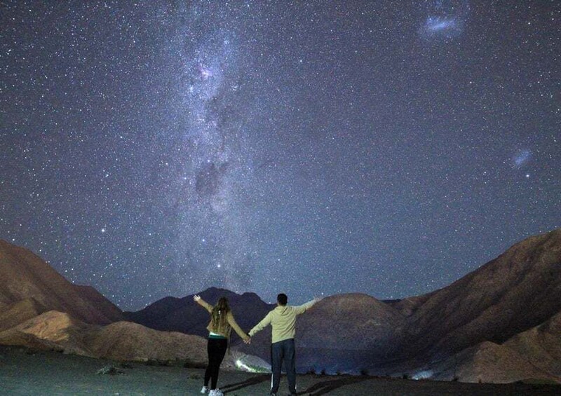Two people standing on a bridge under a starry night sky with the Milky Way visible. 3