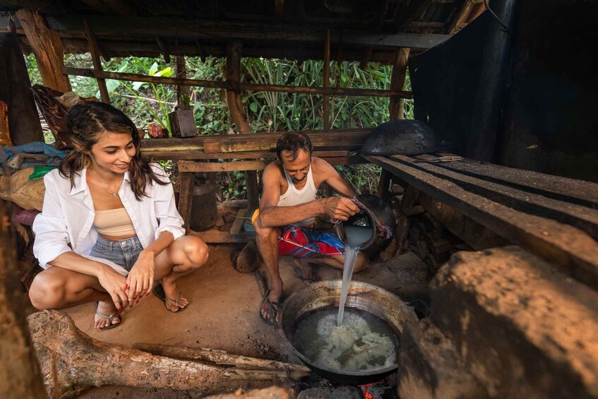 Two people sitting on the ground near a cooking area with a large pot of boiling water. 3