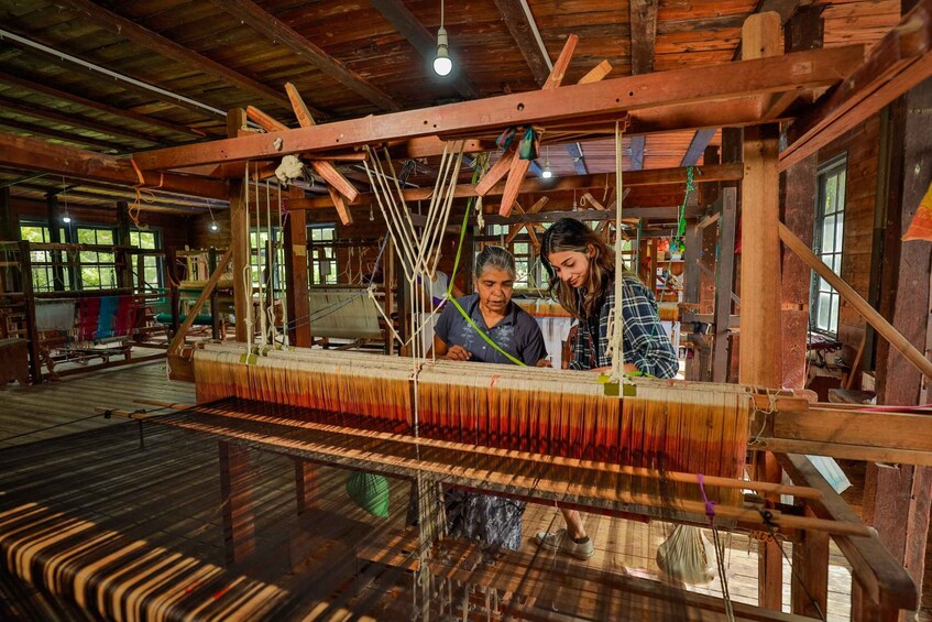 A traditional weaving loom with two people working on it. 2