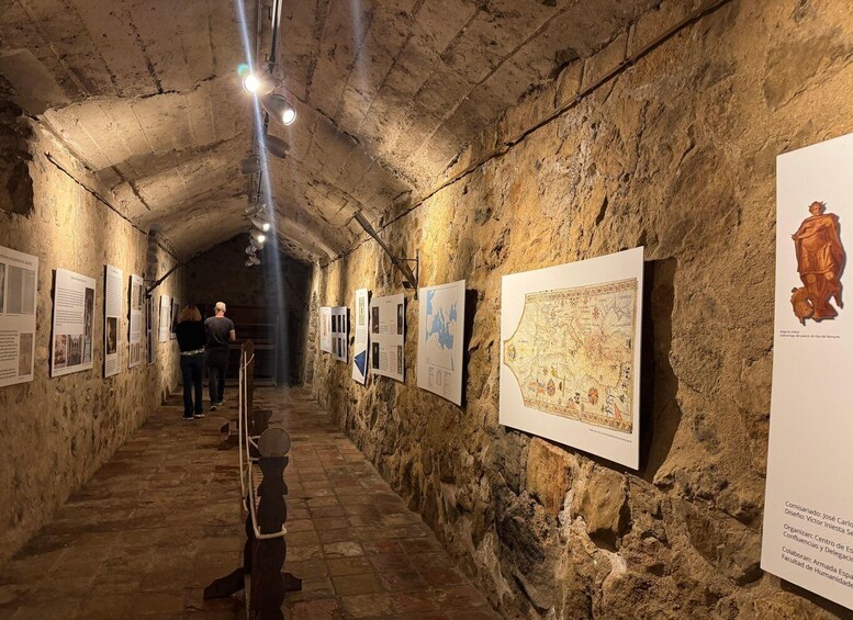 A stone-walled corridor with historical exhibits and a map. 4