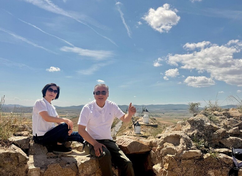 Two people sitting on rocks with a windmill and landscape in the background. 5