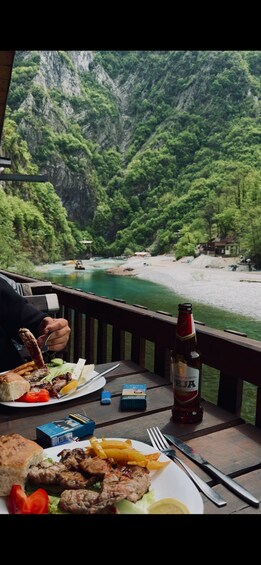 A meal on a wooden deck overlooking a river with a mountainous backdrop. 2
