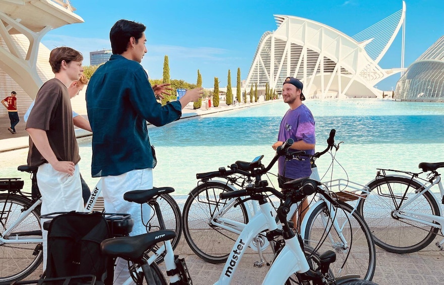 A group of people near a waterfront with bicycles and a modern architectural structure in the background. 5
