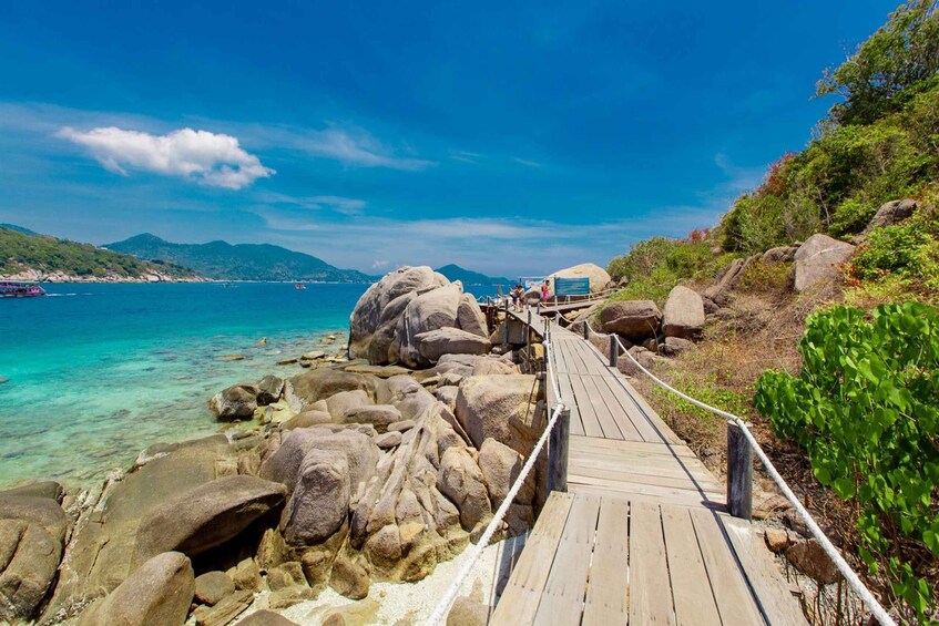 A wooden boardwalk along a rocky coastline with clear turquoise water and distant mountains. 3