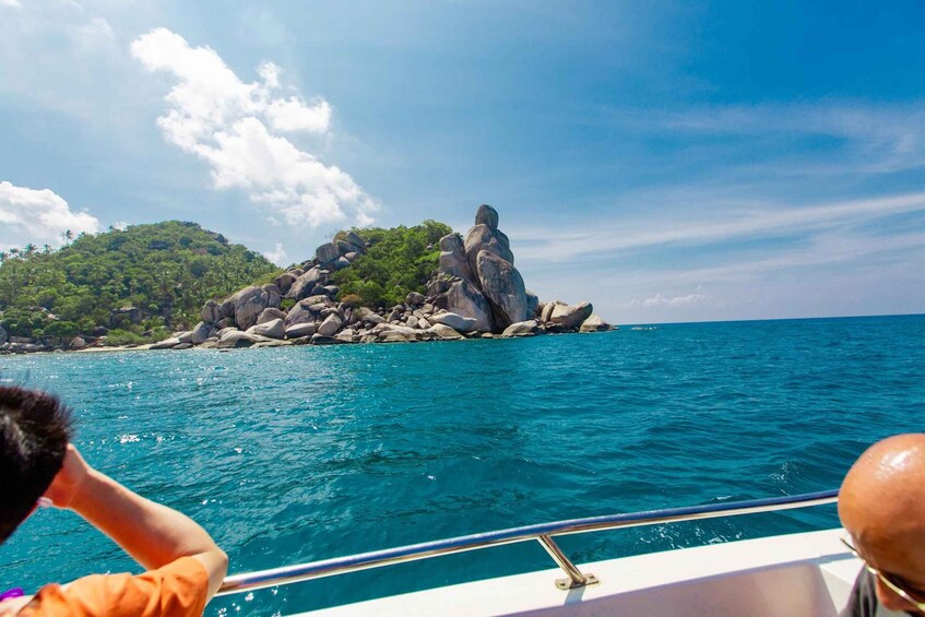A boat on turquoise water with a rocky island and green vegetation in the background. 2