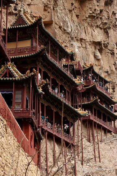 A traditional multi-tiered pagoda with ornate roofs and red pillars, built into a rocky cliffside. 5