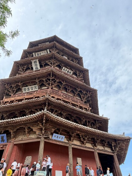 A traditional multi-tiered wooden pagoda with inscriptions, surrounded by tourists. 2