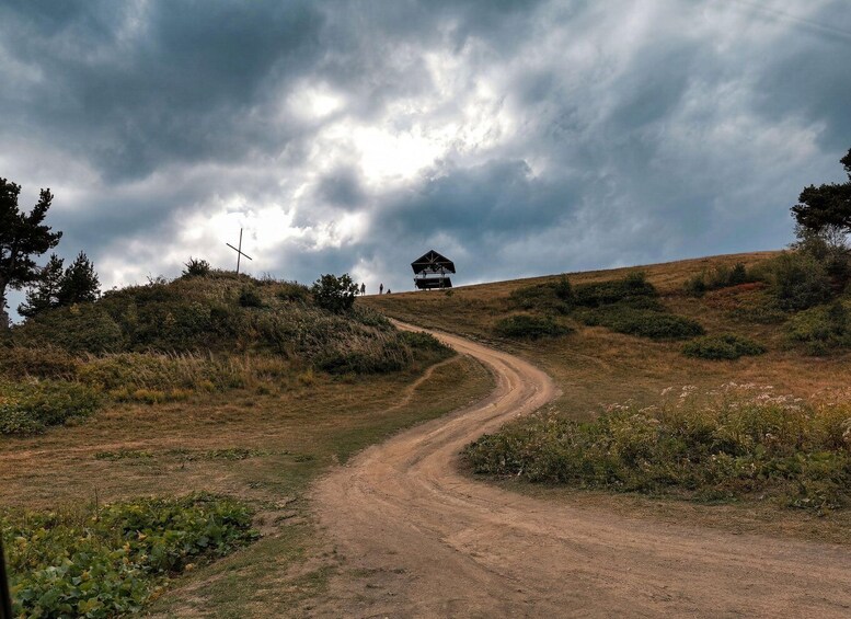 A dirt road winding through a hilly landscape with a small shelter and a cross on a hill. 3