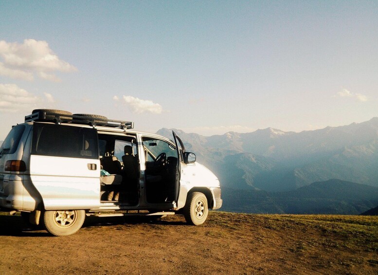 A white van parked on a dirt road with mountains in the background. 4