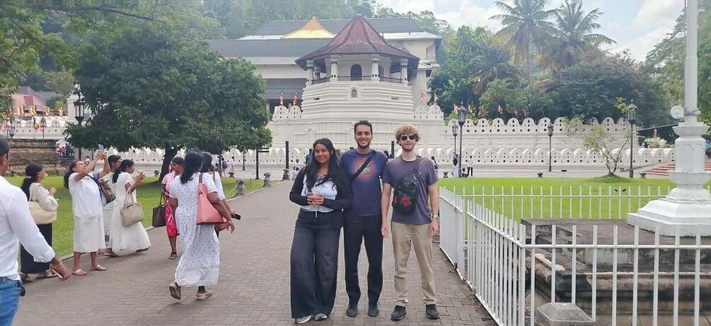 A group of people standing in a park with a white fence and a building with a red roof in the background. 4