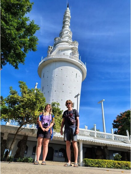 A tall, white tower with a spiral staircase, surrounded by trees and a clear blue sky. 1