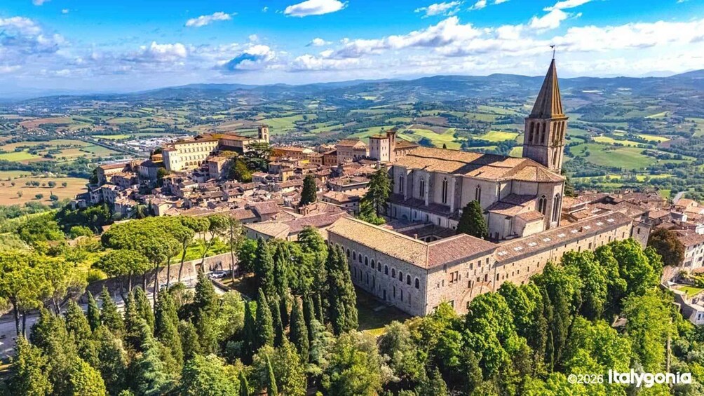 A historic town with a prominent church featuring a tall spire, surrounded by lush greenery and rolling hills in the background. 2