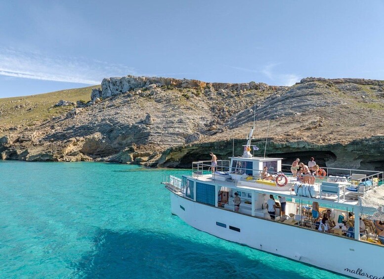 A boat with people on a clear turquoise sea, rocky cliffs in the background. 1