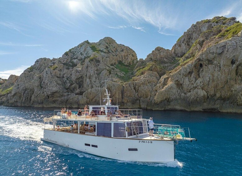 A white boat with people on deck, sailing near rocky cliffs. 3