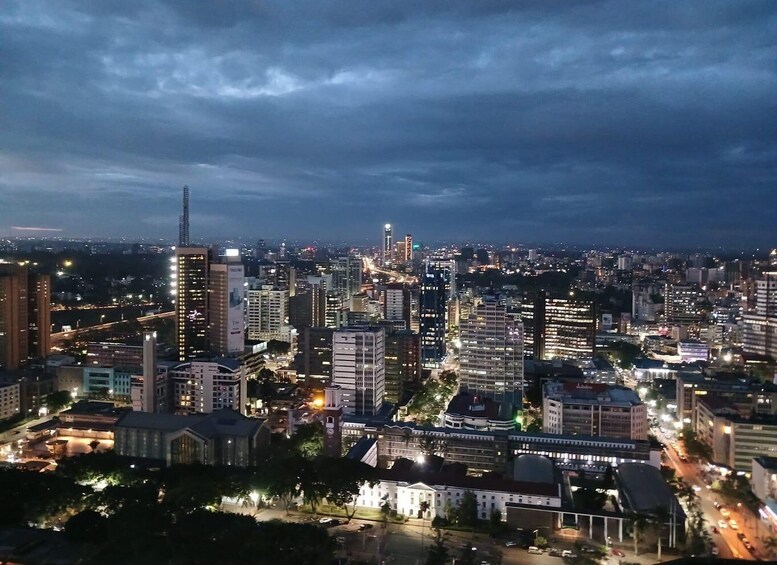 A cityscape at dusk with illuminated buildings and a cloudy sky. 1