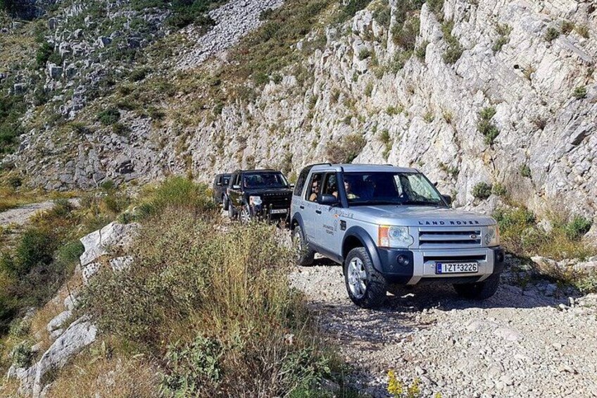 En kuperad terräng med en Land Rover-SUV och ett mindre fordon på en grusväg. 1