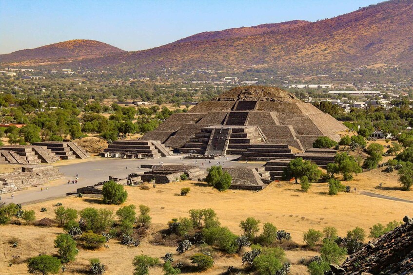 A large pyramid complex with surrounding structures, set against a backdrop of hills and a town. 1
