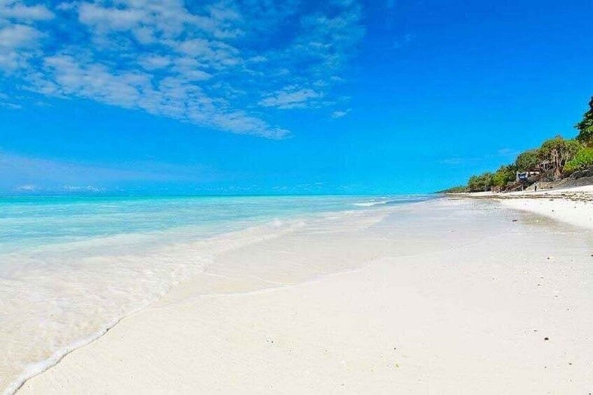 A beach with clear turquoise water, white sand, and a clear blue sky. 1