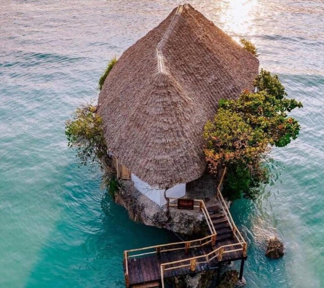 An overwater bungalow with a thatched roof, surrounded by turquoise waters. 4